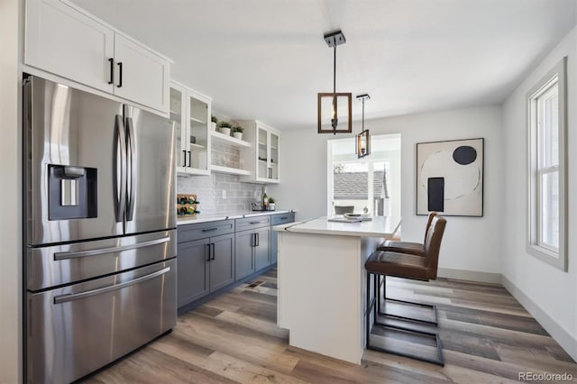 kitchen featuring stainless steel fridge with ice dispenser, glass insert cabinets, wood finished floors, light countertops, and backsplash