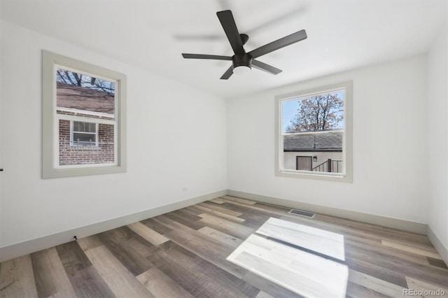 empty room with ceiling fan, wood finished floors, visible vents, and baseboards