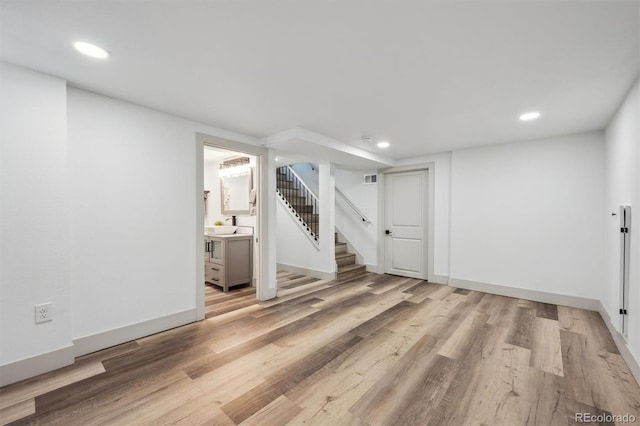 finished below grade area with light wood-type flooring, stairs, and recessed lighting