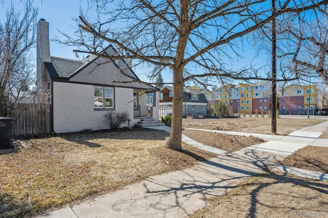 view of front of home featuring roof with shingles, brick siding, a chimney, and a residential view