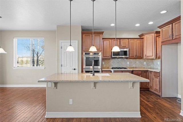 kitchen with tasteful backsplash, a center island with sink, a breakfast bar, brown cabinets, and appliances with stainless steel finishes