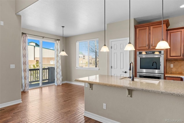 kitchen featuring a wealth of natural light, a kitchen bar, dark wood-type flooring, backsplash, and double oven