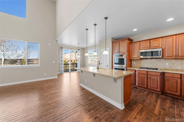 kitchen featuring backsplash, dark wood-type flooring, a center island with sink, stainless steel appliances, and a sink