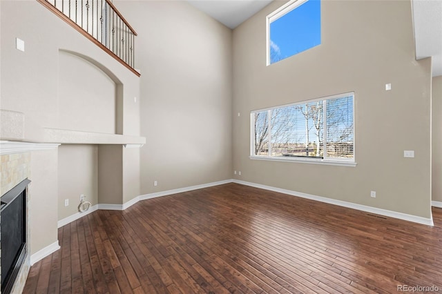 unfurnished living room featuring a towering ceiling, baseboards, hardwood / wood-style floors, and a fireplace