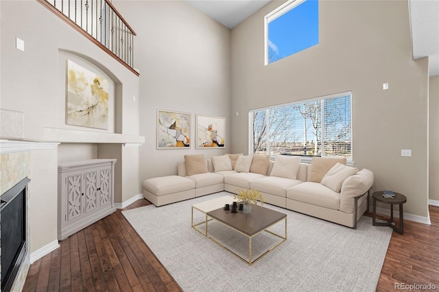 living area featuring a high ceiling, a brick fireplace, baseboards, and wood-type flooring