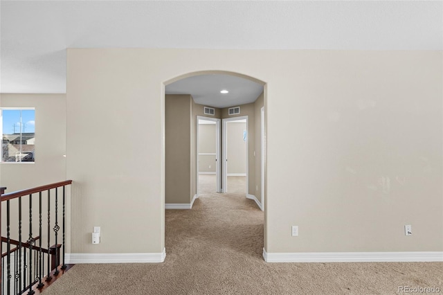 hallway featuring visible vents, carpet, arched walkways, and baseboards