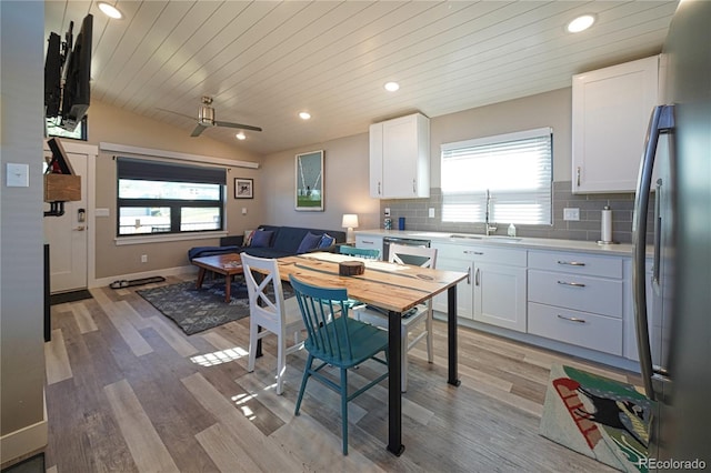 kitchen with stainless steel refrigerator, light countertops, vaulted ceiling, a sink, and tasteful backsplash