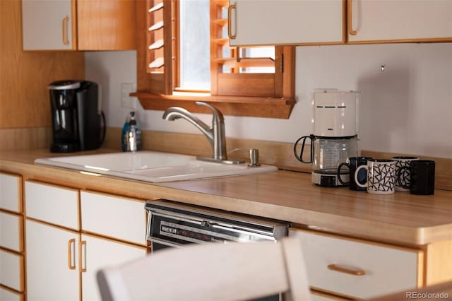 kitchen featuring white cabinets, dishwashing machine, and sink