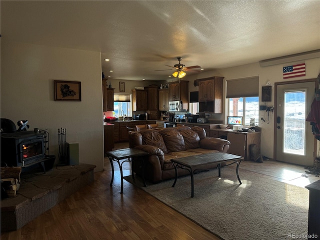 living room with a wood stove, sink, ceiling fan, a textured ceiling, and wood-type flooring