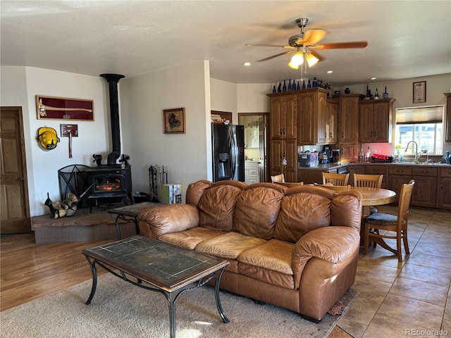 living room with a wood stove, sink, ceiling fan, a textured ceiling, and light hardwood / wood-style floors