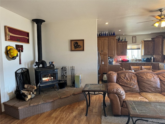 living room featuring a wood stove, ceiling fan, sink, and light wood-type flooring