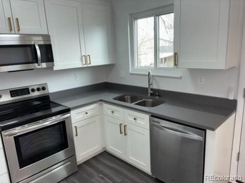 kitchen featuring dark wood-style flooring, dark countertops, white cabinetry, a sink, and stainless steel appliances