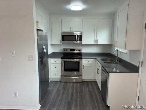 kitchen with a sink, dark countertops, stainless steel appliances, and white cabinetry