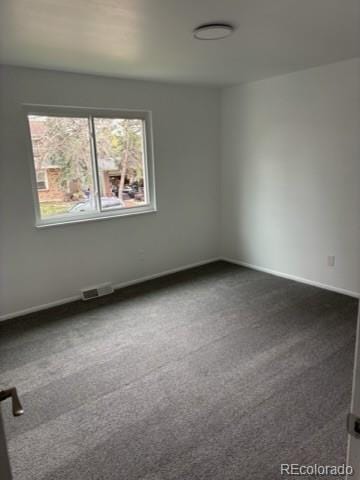 unfurnished room with visible vents, a wealth of natural light, and dark colored carpet