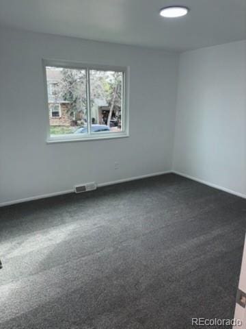 unfurnished room featuring baseboards, dark carpet, and visible vents