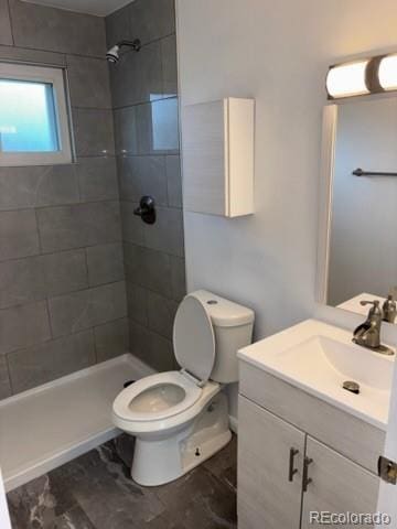 bathroom featuring toilet, a tile shower, and vanity