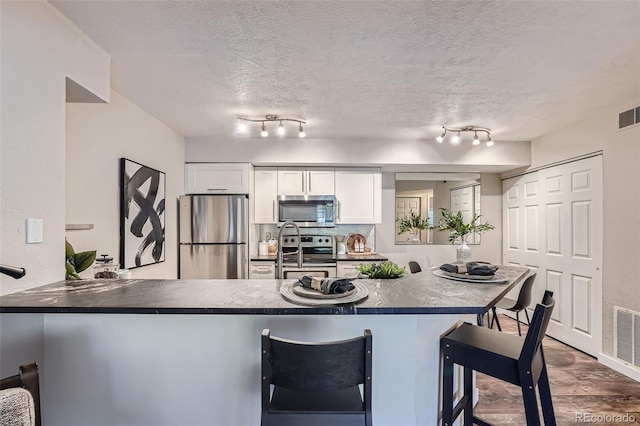 kitchen featuring kitchen peninsula, a kitchen breakfast bar, stainless steel appliances, white cabinets, and track lighting