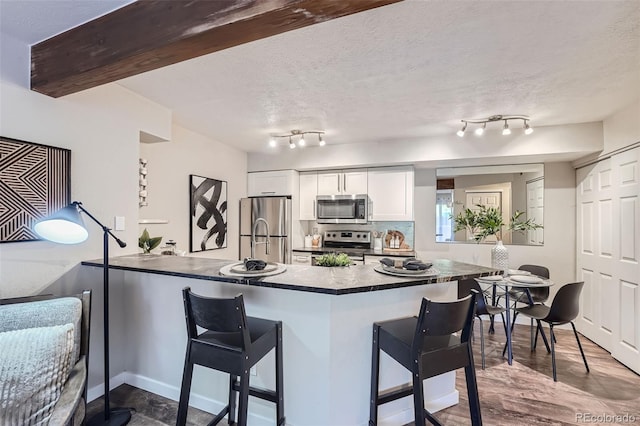 kitchen with kitchen peninsula, appliances with stainless steel finishes, white cabinetry, a kitchen bar, and dark wood-type flooring