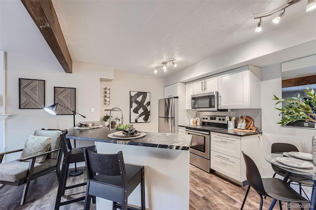 kitchen with wood-type flooring, white cabinetry, stainless steel appliances, beam ceiling, and a breakfast bar area