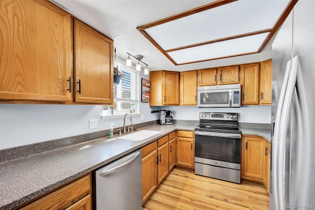 kitchen with a sink, stainless steel appliances, brown cabinets, and light wood-style floors