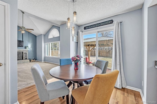 dining space featuring lofted ceiling, a textured ceiling, a fireplace, baseboards, and ceiling fan