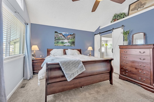 bedroom featuring visible vents, lofted ceiling, a textured ceiling, a barn door, and light colored carpet