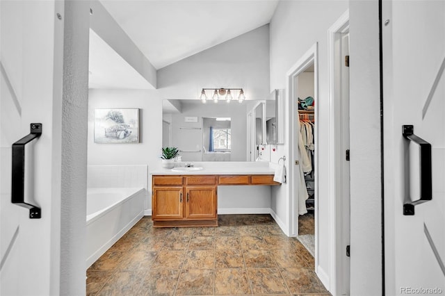 full bath featuring vanity, lofted ceiling, stone finish flooring, a walk in closet, and a garden tub