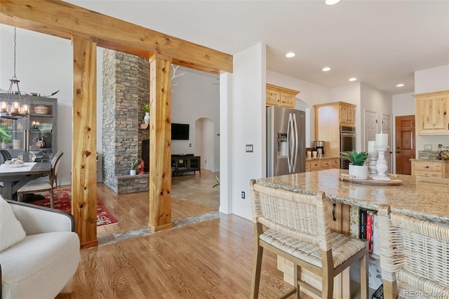 2467 Spanish Oak Ter, Colorado Springs, CO 80920 - kitchen featuring arched walkways, stainless steel appliances, light wood-style floors, light stone countertops, and a breakfast bar