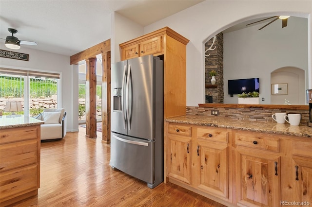 2467 Spanish Oak Ter, Colorado Springs, CO 80920 - kitchen featuring stainless steel refrigerator with ice dispenser, ceiling fan, arched walkways, light wood finished floors, and light stone counters