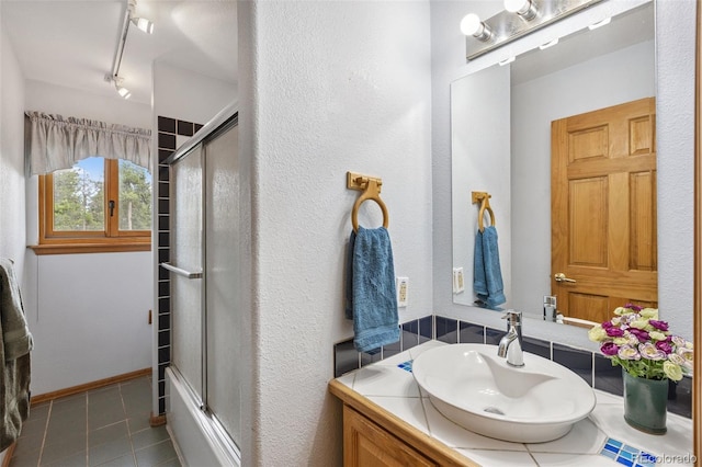 10668 Crystal Way, Morrison, CO 80465 - full bath with vanity, tile patterned floors, rail lighting, bath / shower combo with glass door, and a textured wall