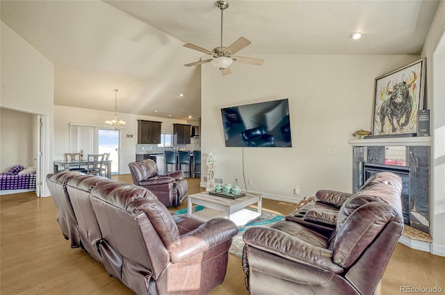 living room with light hardwood / wood-style floors, ceiling fan with notable chandelier, and vaulted ceiling