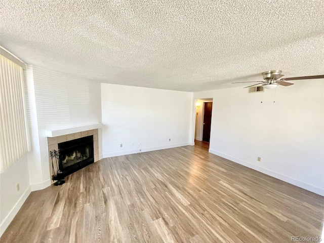 unfurnished living room with ceiling fan, light hardwood / wood-style floors, a textured ceiling, and a tiled fireplace