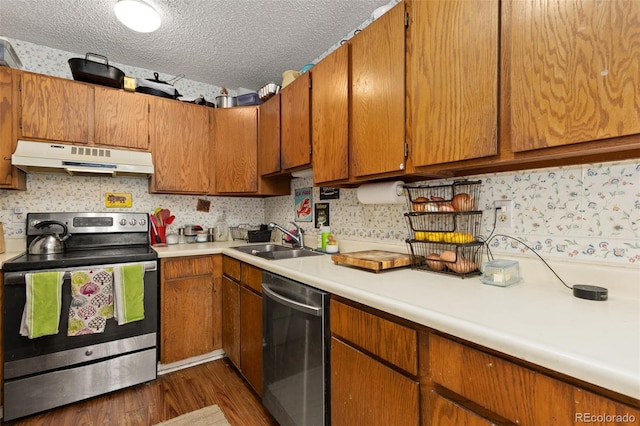 kitchen with light countertops, appliances with stainless steel finishes, a sink, a textured ceiling, and under cabinet range hood