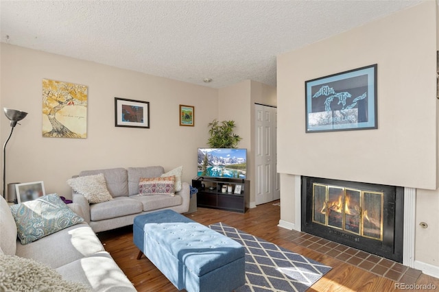 living area featuring baseboards, dark wood finished floors, a textured ceiling, and a glass covered fireplace