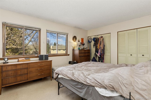 bedroom featuring a textured ceiling, light colored carpet, and multiple closets