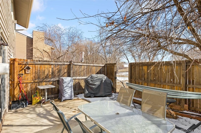 snow covered patio featuring outdoor dining area, fence, and grilling area