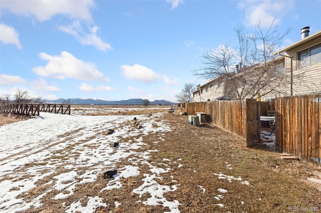 yard covered in snow with a mountain view and fence