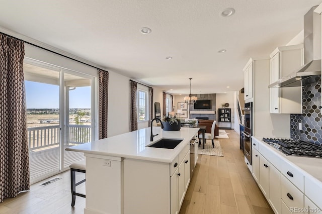 kitchen with a kitchen island with sink, sink, wall chimney exhaust hood, decorative light fixtures, and stainless steel appliances