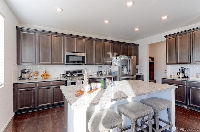 kitchen featuring appliances with stainless steel finishes, a center island with sink, dark brown cabinets, and dark wood-type flooring