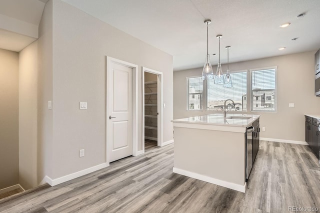 kitchen featuring light wood-style flooring, baseboards, light countertops, hanging light fixtures, and an island with sink