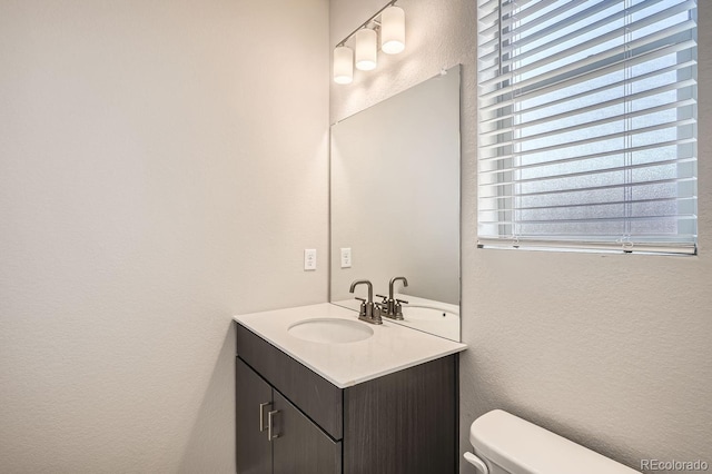 half bathroom featuring toilet, a textured wall, and vanity