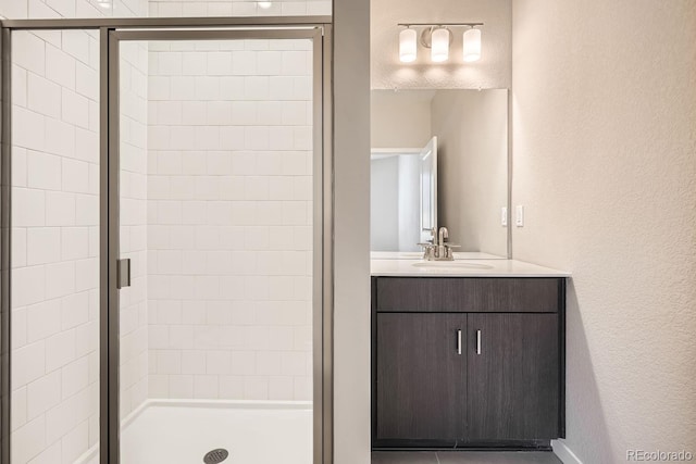 full bath featuring a textured wall, a shower stall, and vanity