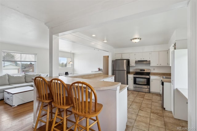 1422 N Chelton Rd, Colorado Springs, CO 80909 - kitchen with stainless steel appliances, under cabinet range hood, light countertops, white cabinets, and a kitchen breakfast bar