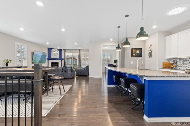 kitchen with white cabinets, dark wood finished floors, light stone countertops, a lit fireplace, and a sink