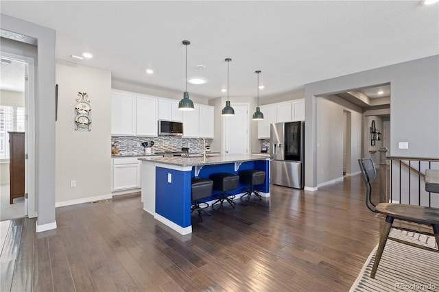 kitchen featuring white cabinets, dark wood finished floors, an island with sink, a breakfast bar, and stainless steel appliances