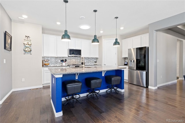 kitchen with white cabinets, light stone counters, stainless steel appliances, a kitchen bar, and a sink