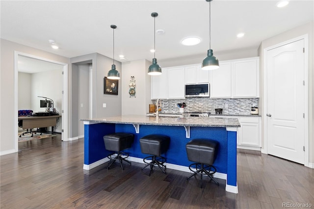 kitchen featuring a sink, backsplash, light stone countertops, stainless steel microwave, and a kitchen bar