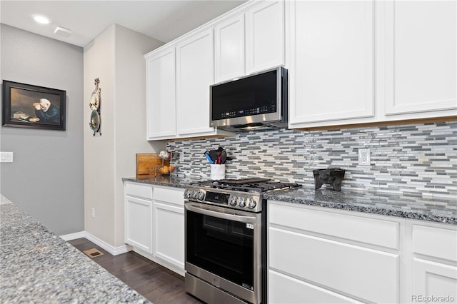 kitchen featuring stainless steel appliances, dark wood-type flooring, dark stone countertops, and decorative backsplash