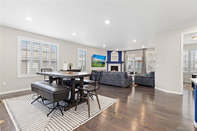 dining room with a wealth of natural light, a warm lit fireplace, recessed lighting, and wood finished floors