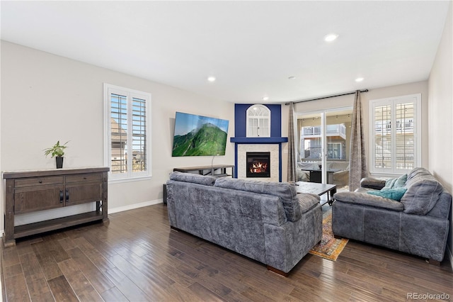 living area featuring a glass covered fireplace, dark wood-style flooring, baseboards, and recessed lighting